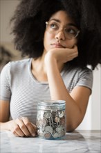 Pensive African American woman with jar full of coins