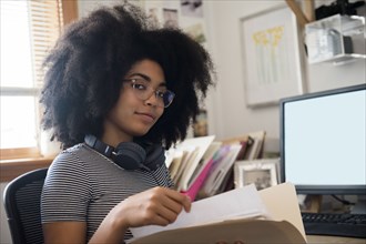 Confident African American woman holding files near computer