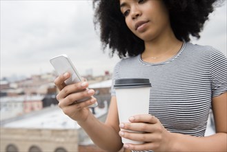 African American woman drinking coffee and texting on cell phone