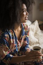 African American woman sitting in bed drinking coffee