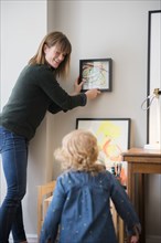 Caucasian mother and daughter hanging painting on wall