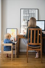 Caucasian mother working and daughter playing in home office