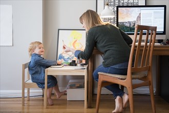 Caucasian mother working and daughter playing in home office