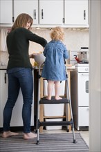 Caucasian girl standing on ladder cooking with mother in kitchen