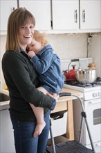 Caucasian mother holding daughter sucking thumb in kitchen