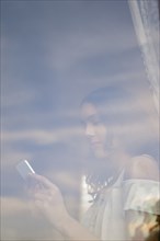 Hispanic woman texting on cell phone behind window