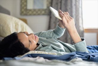 Hispanic woman laying in bed texting on cell phone