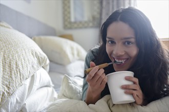 Hispanic woman laying on bed eating ice cream from carton