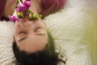 Hispanic woman laying on bed smelling flowers