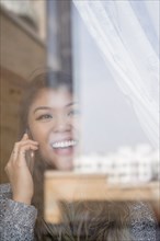 Mixed Race woman talking on cell phone behind window