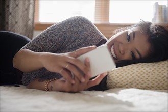 Mixed Race woman laying on bed texting on cell phone