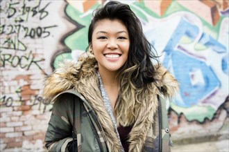 Portrait of smiling Mixed Race woman standing near graffiti