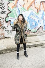 Laughing Mixed Race woman standing near graffiti