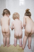 Naked Caucasian boy and girls standing near bathtub