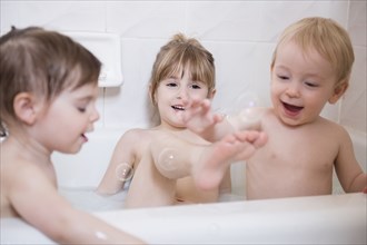 Smiling Caucasian boy and girls playing with bubbles in bathtub