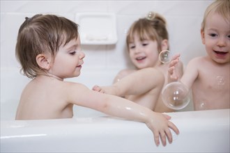 Smiling Caucasian boy and girls playing with bubbles in bathtub