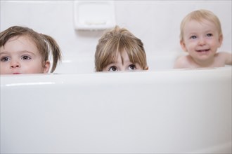 Caucasian boy and girls peaking from bathtub