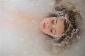 Face of Caucasian girl floating in bubble bath