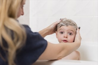 Caucasian mother washing hair of girl in bathtub