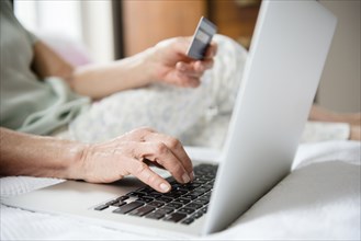 Hands of older woman shopping online with credit card and laptop