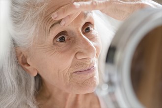 Older woman checking eye wrinkles in mirror