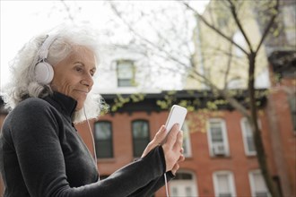 Older woman listening to cell phone with headphones in city
