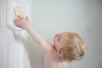 Caucasian baby boy in milk bath reaching for soap