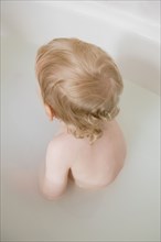Caucasian baby boy sitting in milk bath