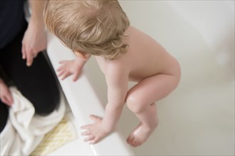 Caucasian baby boy climbing to mother from bathtub