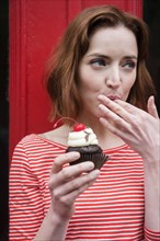 Caucasian woman holding a cupcake licking finger