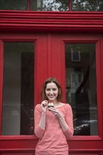 Caucasian woman holding a cupcake near red doorway
