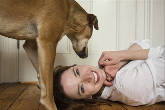 Dog standing over Caucasian woman laying on floor