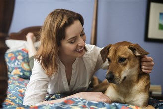 Caucasian woman and dog laying on bed