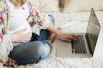 Caucasian and expectant mother using laptop on bed