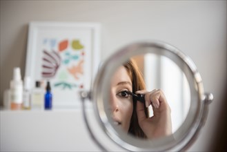 Reflection of Caucasian woman applying mascara in mirror