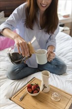 Caucasian woman sitting in bed pouring coffee
