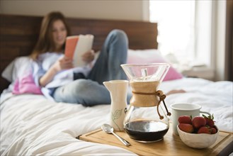 Caucasian woman laying in bed reading book near breakfast tray