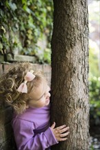 Caucasian girl hiding behind tree trunk