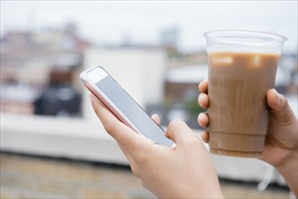 Hands of African American woman drinking coffee and texting on cell phone