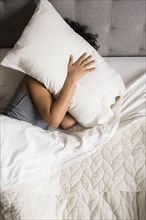 African American woman laying on bed hiding face under pillow