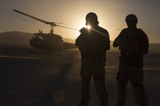 Silhouette of soldiers watching helicopter in desert landscape