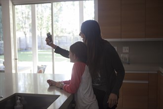 Mixed race mother and daughter taking selfie in kitchen