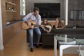 Father playing guitar for daughters in living room
