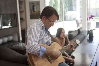 Father playing guitar for daughter in living room