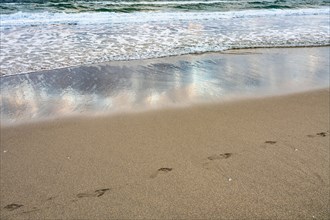 Footprints and sea wave on sandy beach