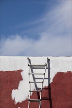 Ladder against partially painted brown and white wall