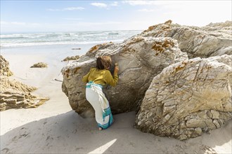 Boy hiding behind rock on beach