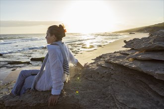 Girl sitting on beach at sunset