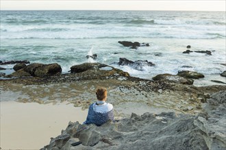 Girl sitting on beach looking at ocean