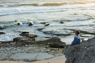 Girl sitting on beach looking at ocean